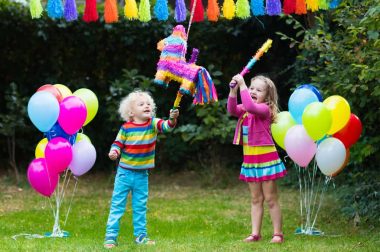Kids birthday party. Group of children hitting pinata and playing with balloons. Family and friends celebrating birthday outdoors in decorated garden. Outdoor celebration with active games.