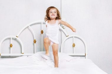 Active toddler girl dancing in bed