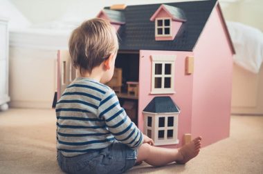 A cute gender confident little boy is busting stereotypes and socially imposed expectations by playing with a big pink doll house and having a great time
