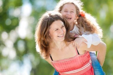 Beautiful and happy young mother giving piggyback ride to her laughing daughter